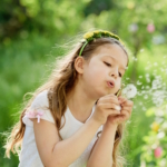 girl blowing dandelions flower selective focus. Allergy season.